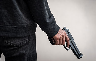 Person holding a handgun behind their back, representing violent crimes.