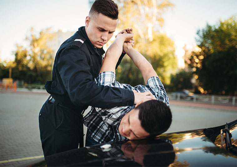 Police officer arresting a man by holding his arm over a car, representing criminal defense